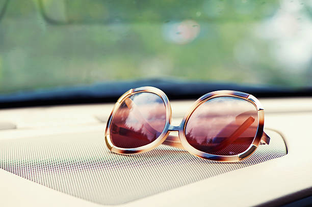 Elegant fashionable plastic women's sunglasses on interior car dashboard. Indoors close-up.