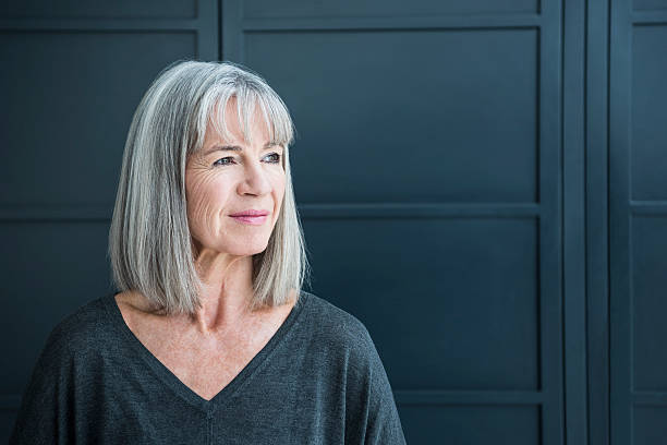 Senior woman with gray hair looking away One senior woman with a grey bob in front of a dark grey background. Portrait of smart senior woman in her 60s, looking away from camera. grey hair stock pictures, royalty-free photos & images