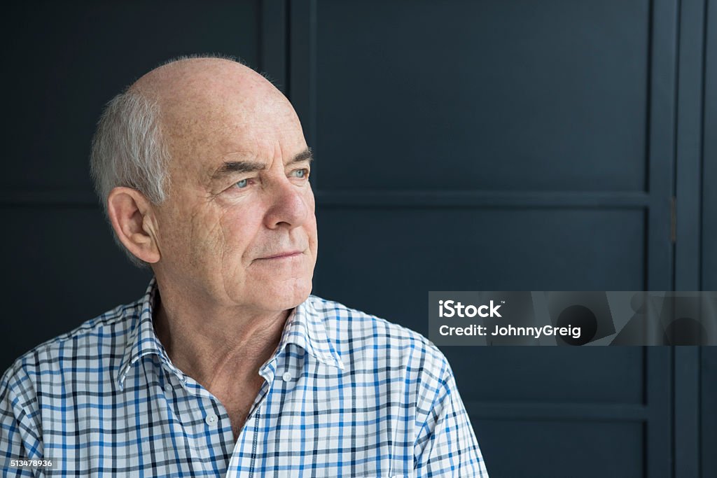 Senior man in his 70s looking away against grey background Portrait of a senior man in checked shirt, looking away from camera. He is in front of a gray background with a pensive expression on his face. Senior Men Stock Photo
