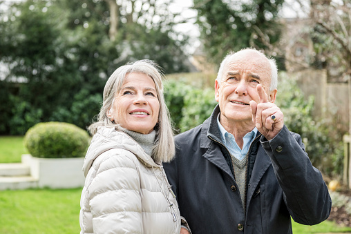 Senior man and woman looking away, the man is pointing his finger. Two senior adults in a garden in warm jackets.