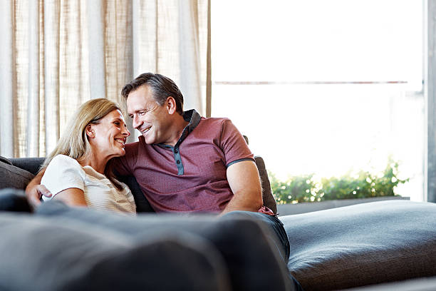 Canoodling on the couch Shot of an affectionate mature couple relaxing together on their living room sofa canoodling stock pictures, royalty-free photos & images