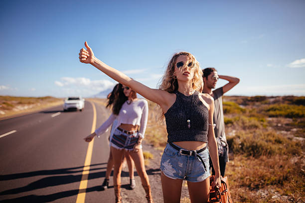 Hipster Multi-Ethnic Group of friends Hitchhiking on Highway Hipster multi-ethnic group of friends hitchhiking on two lane highway in the sunshine with thumb sticking out and suitcase in hand hitchhiking stock pictures, royalty-free photos & images