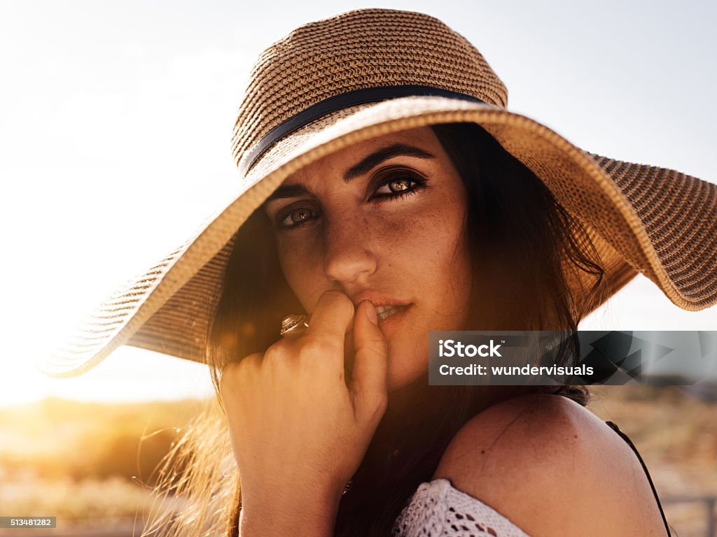 Hipster Girl close up on Sandy Beach Close up of hipster girl in large brimmed hat looking provocatively with hand touching mouth at camera Beauty Stock Photo