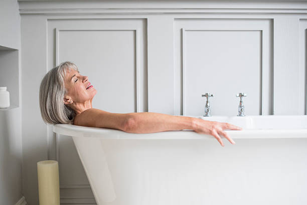 senior frau entspannung in bad mit augen geschlossen - bathtub women relaxation bathroom stock-fotos und bilder