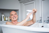 Senior man in bath washing himself smiling
