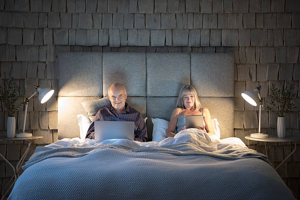 starsza para w łóżku nocą z laptopa i tabletki - couple laptop computer digital tablet zdjęcia i obrazy z banku zdjęć