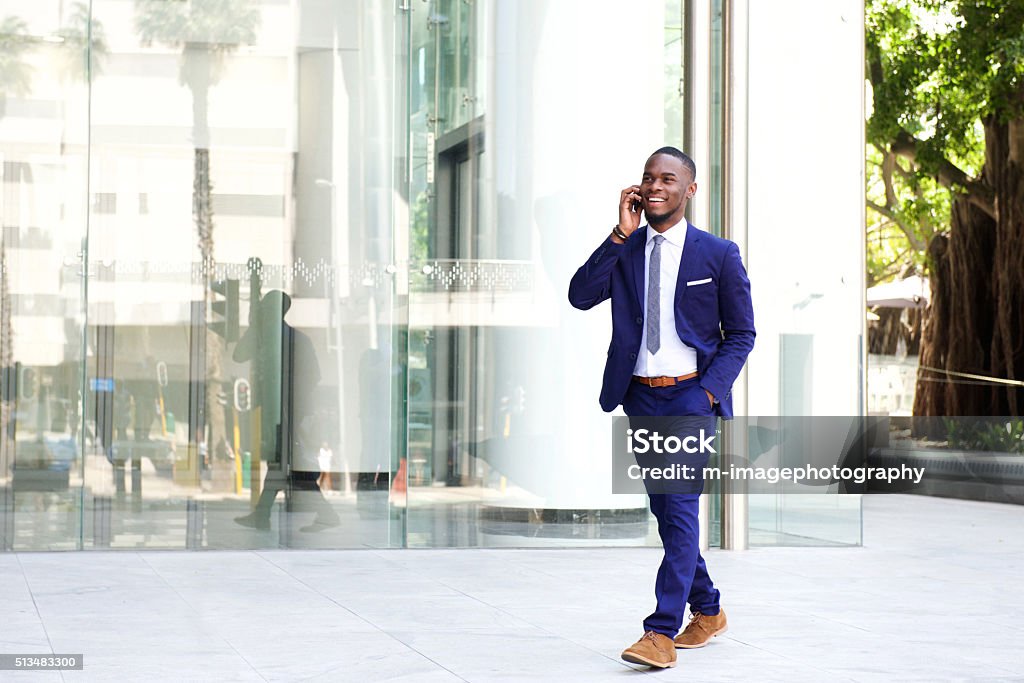 Businessman walking in the city using mobile phone Full length portrait of a happy young businessman walking in the city and talking on mobile phone Walking Stock Photo