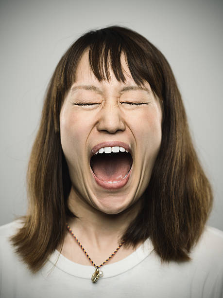 Portrait of a young japanese woman screaming. Studio portrait of a japanese young woman screaming. The woman is around 30 years and has long hair and casual clothes. Vertical color image from a medium format digital camera. Sharp focus on eyes. mouth open human face shouting screaming stock pictures, royalty-free photos & images