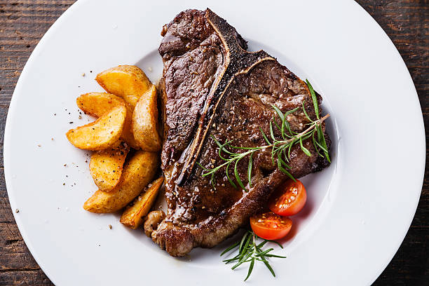 Grilled T-Bone Steak with roasted potato wedges Grilled T-Bone Steak with roasted potato wedges on white plate on wooden background close up t bone steak stock pictures, royalty-free photos & images