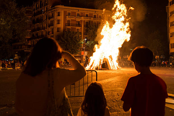 Family looking at a bonfire at night to celebrate the festivity of Sant Joan on a street in Barcelona, Catalonia, Spain