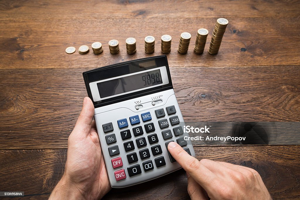 Businessman Doing Calculations Businessman Doing Calculations In Front Of Stacked Coins Adult Stock Photo