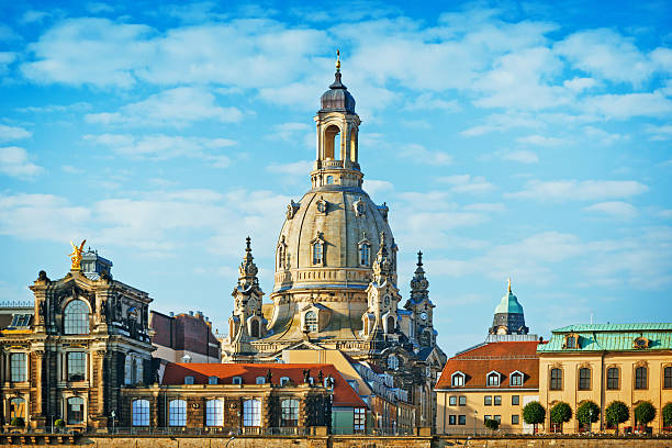 Low-angle view of the Fürstenzug (Procession of Princes, ca. 1907) on the outer wall of the Castle and Courthouse in Dresden, Germany, with the dome of the Frauenkirche in the background.