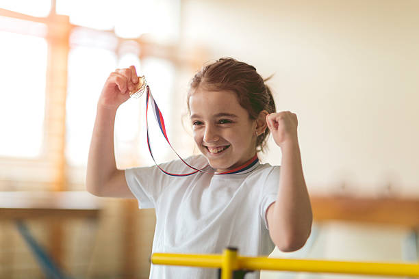 Cute little girl high jumper posing with her gold medal. She is happy and cheerful.
