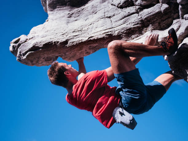Bouldering rock climber hanging beneath extreme overhang against blue sky