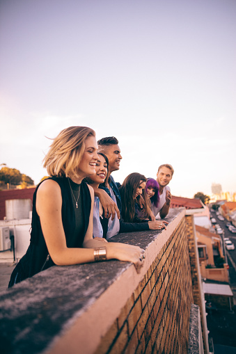 Group of multi-ethnic teenager friends leaning on the parapet of a  rooftop laughing and chatting