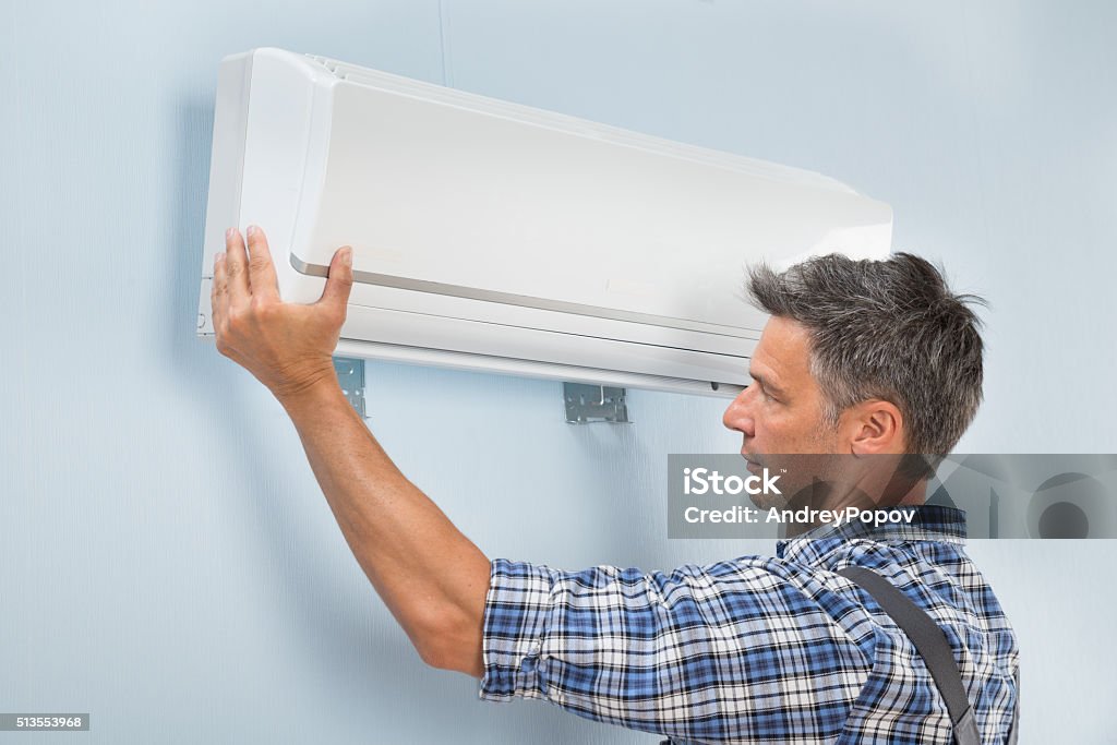 Male Technician Fixing Air Conditioner Portrait Of A Mid-adult Male Technician Fixing Air Conditioner On Wall Adult Stock Photo