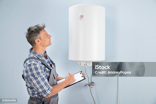 Male Plumber With Clipboard Looking At Electric Boiler Stock Photo - Download Image Now