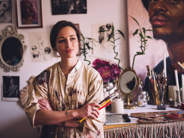 istock Artist in her studio wearing paint covered smock with paintbrush 513556814