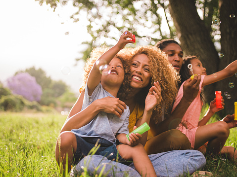 Young african-american family sharing a special moment in the sun blowing colouful soap bubbles and laughing toghether cheerfully.