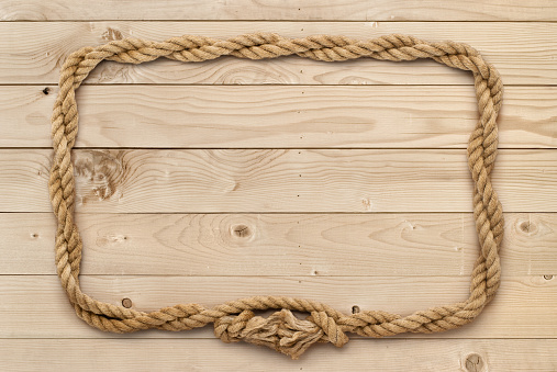 Rope frame on nature beige wooden board. The rope is twisted and bent into a rectangular shape. Weathered light brown wooden board is composed of seven panels. A wood grain pattern featuring even grains of wood running horizontally across the image. Compounds of the boards are clearly visible.
