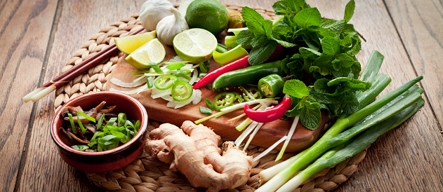 Ingredients for spicy thai and vietnamese soup Tom Yam. All board contains fresh spring onions, shallots, lemongrass, ginger, garlic, chili, mint leaves, shiitake mushrooms cilantro leaves.