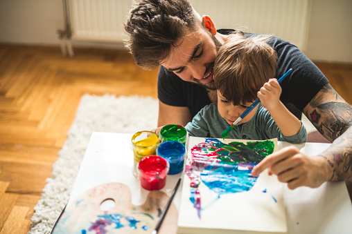 Man learning his cute son how to paint.