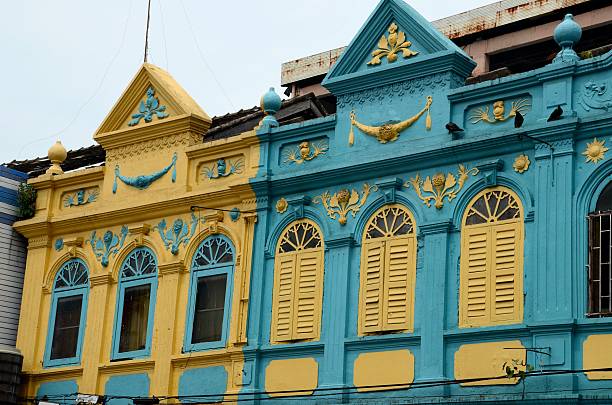 Hat Yai, Thailand - August 30, 2015: Two peranakan style designed houses on a street in Hat Yai, southern Thailand's Songkhla province. The style reflected the mixed influences among Chinese immigrants, including traditional Chinese, colonial, Malay and local Thai influences. Note the arched windows with wood shutters and the designs above windows.
