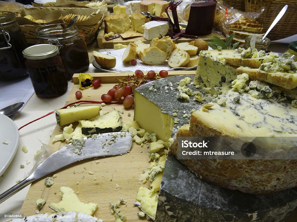 Stack of cheeses / Stilton, Cornish-Yarg cheese cake on wooden board Photo showing a small stack of cheeses - a real cheese cake, displayed on a wooden breadboard with red and green grapes, sliced fresh figs, chutneys and pickles, sliced white bread, crackers / biscuits, and a sprig or two of rosemary herb.  The round cheeses are Cornish Yarg (low-fat, wrapped in stinging nettle leaves) and Colston Basset (a mature Blue Stilton cheese).  This attractive, savoury cake made with cheese featured more tiers (brie and Cheddar) that were quickly eaten and is becoming a popular alternative to the more traditional iced, tiered wedding cakes. Baguette Stock Photo