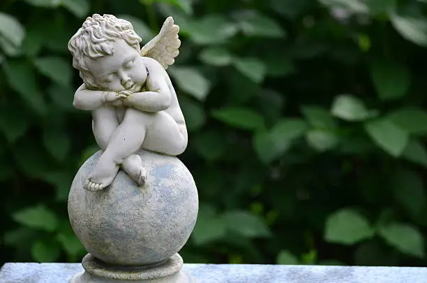 Photo of Child angel statue sitting on a gravestone in the cemetery