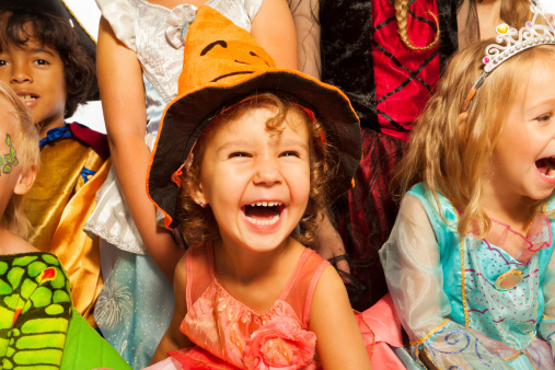 Little laughing girl wearing dress and Halloween hat surrounded by friends kids, close-up studio portrait
