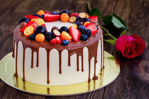 Chocolate cake with various berries and rose on wooden table