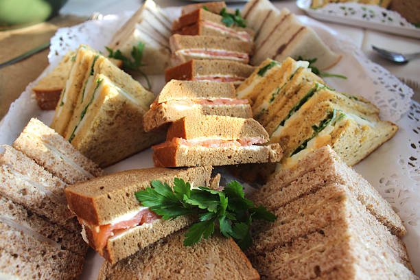 Photo showing a sandwich platter made using freshly baked brown granary bread and white bread.  The triangular sandwiches are being served as part of a party food / finger-food buffet and include ham, cheese, smoked salmon and cream cheese, beef and horseradish, and egg salad, cress and lettuce - looking rather like they could be served as part of a traditional afternoon tea.