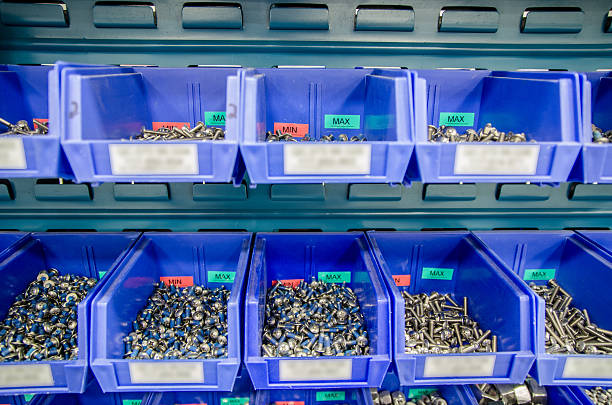 Rows of blue plastic storage bins containing stocks of parts and components, such as screws, bolts and nuts, in an industrial or commercial warehouse shot with selective focus. This folllows the 5S (Lean or just in time) methods with the minimum and maximum marks at the end of the bins.