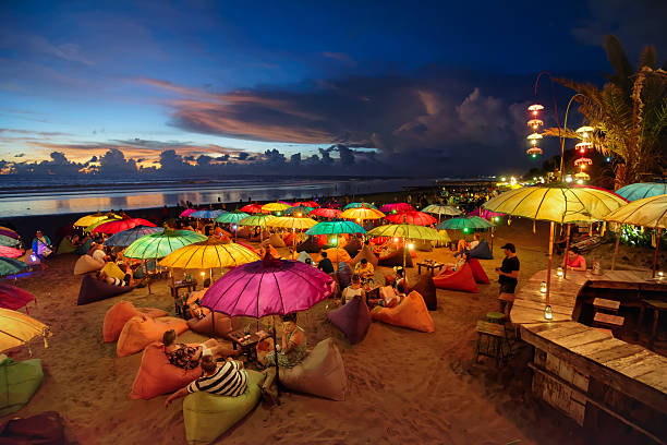 Seminyak beach at dusk Seminyak, Indonesia - February 25, 2016: Seminyak beach at dusk. People chilling out, having drinks, laying on puffs, under colourful lit parasols bali stock pictures, royalty-free photos & images