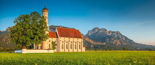 Panoramic view of famous St. Coloman church with scenic Neuschwanstein Castle in the background in beautiful evening light at sunset in summer, Schwangau, Fussen, Bavaria, Germany