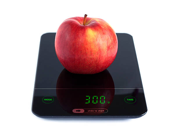 Big tasty red apple on kitchen scales isolated on white background. Front view closeup