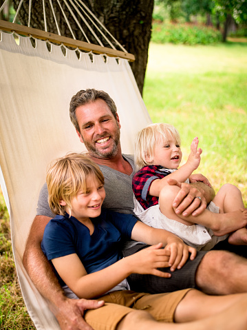 Modern father relaxing and enjoying quality time with his two blonde sons outside on a hammock