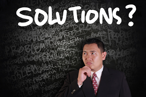 Problems and Solutions Concept, Asian businessman thinking of solutions with problems words on chalk board around him
