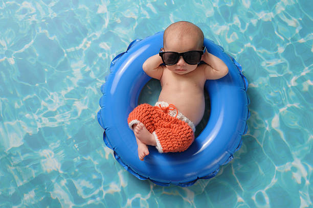 Newborn Baby Boy Floating on an Inflatable Swim Ring Four week old newborn baby boy sleeping on a tiny inflatable swim ring. He is wearing crocheted board shorts and black sunglasses. inflatable ring photos stock pictures, royalty-free photos & images