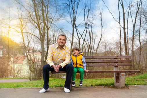 father and little boy on bench in park smiling.