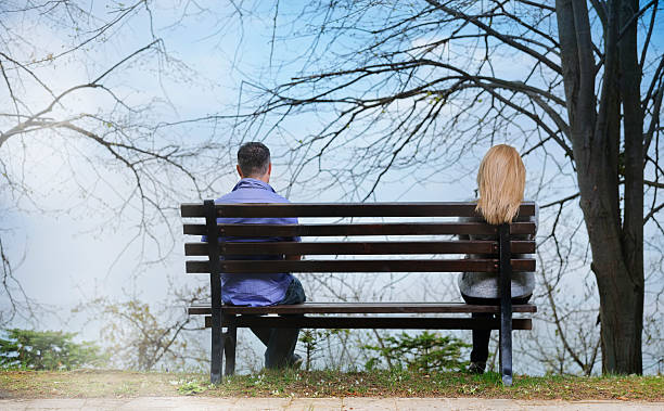 sadness today rear view of couple with relationship difficulties sitting on bench. sitting on bench stock pictures, royalty-free photos & images