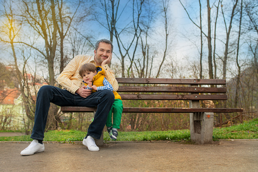 father and little boy in park on bench.
