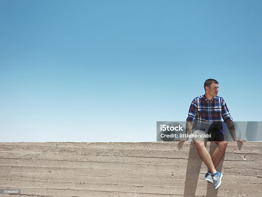 Man sitting on the wall Man sitting on on the top of concrete wall Accuracy Stock Photo