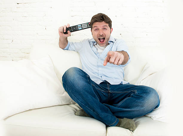 istock young happy man watching television smiling and laughing in sofa 513679096
