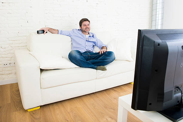 istock young happy man watching television smiling and laughing in sofa 513679998
