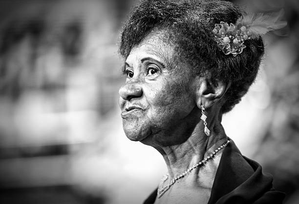 Elderly black lady with grey Afro hair looking into camera with green cardigan