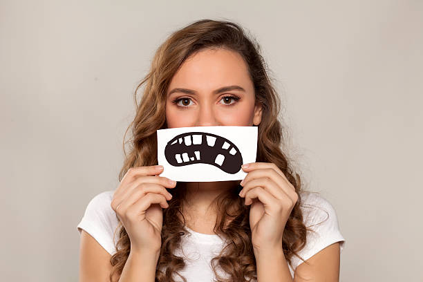 dental problem sad girl holding a defective teeth drawn on a sheet of paper over her mouth bad teeth stock pictures, royalty-free photos & images