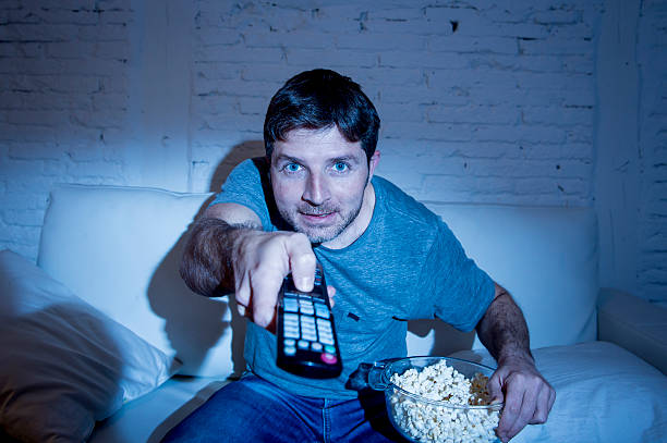 istock man watching television sports eating popcorn bowl using remote control 513684560