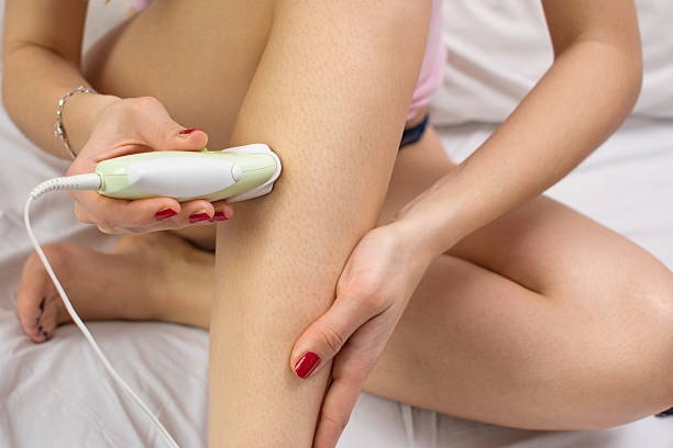 Girl epilates her leg with an epilator Girl epilates her leg with an epilator on the bed epilator stock pictures, royalty-free photos & images