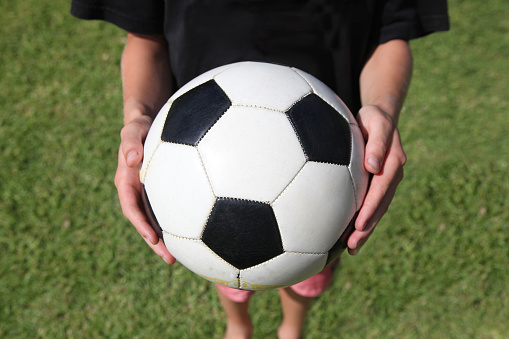 A boy holds a soccer ball above green grass